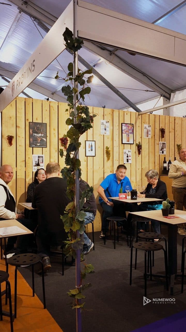 Stand de Provins habillé de planches de bois et de vigne, avec des visiteurs attablés, à la Foire du Jura