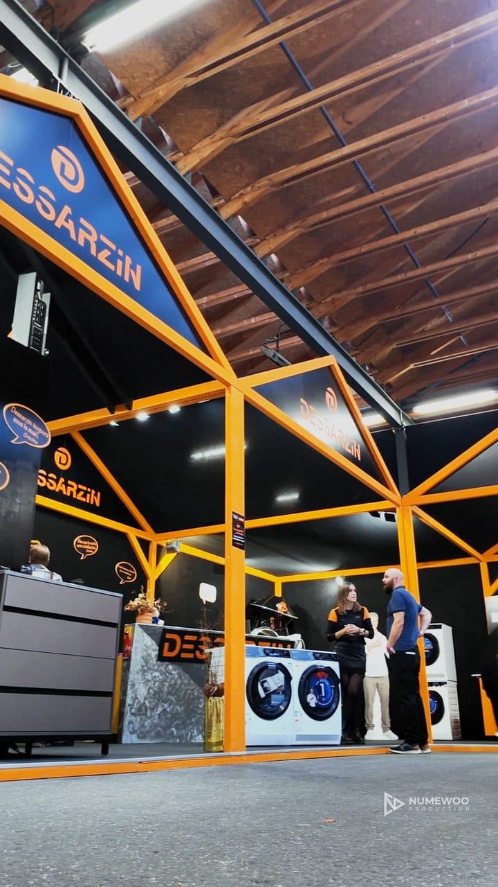 Lave-linge orange entouré de pièces détachées et d'un multimètre, sur le stand de Dessarzin Électroménager