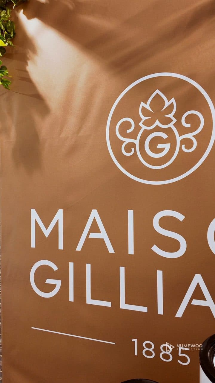 Visiteurs attablés sur le stand de la Maison Gilliard, moquette violette et drapeaux valaisans, à la Foire du Jura